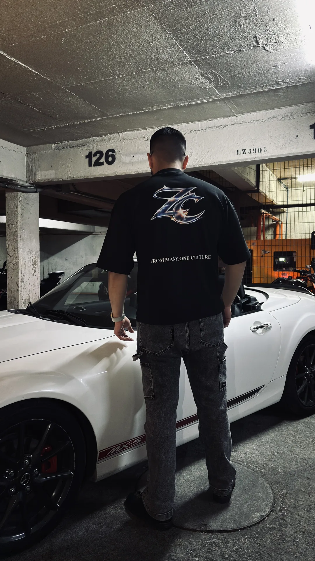 Modelo de espaldas mostrando el estampado trasero de la polera junto al auto